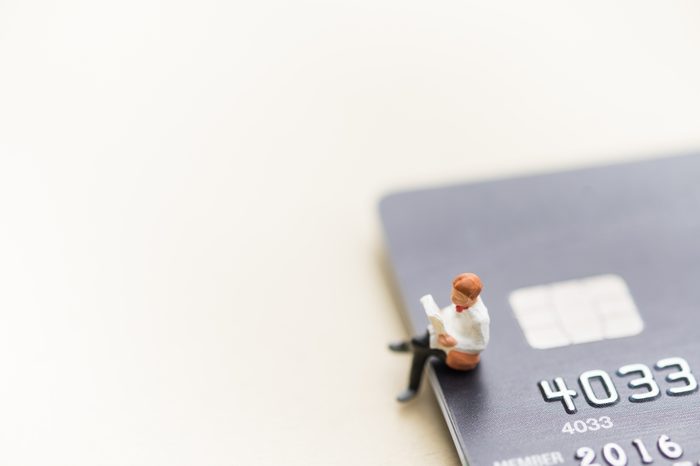 Finance, Business, Shopping and e-commerce concept. Close up of man miniature figure toy sit and read a book on stack of credit cards