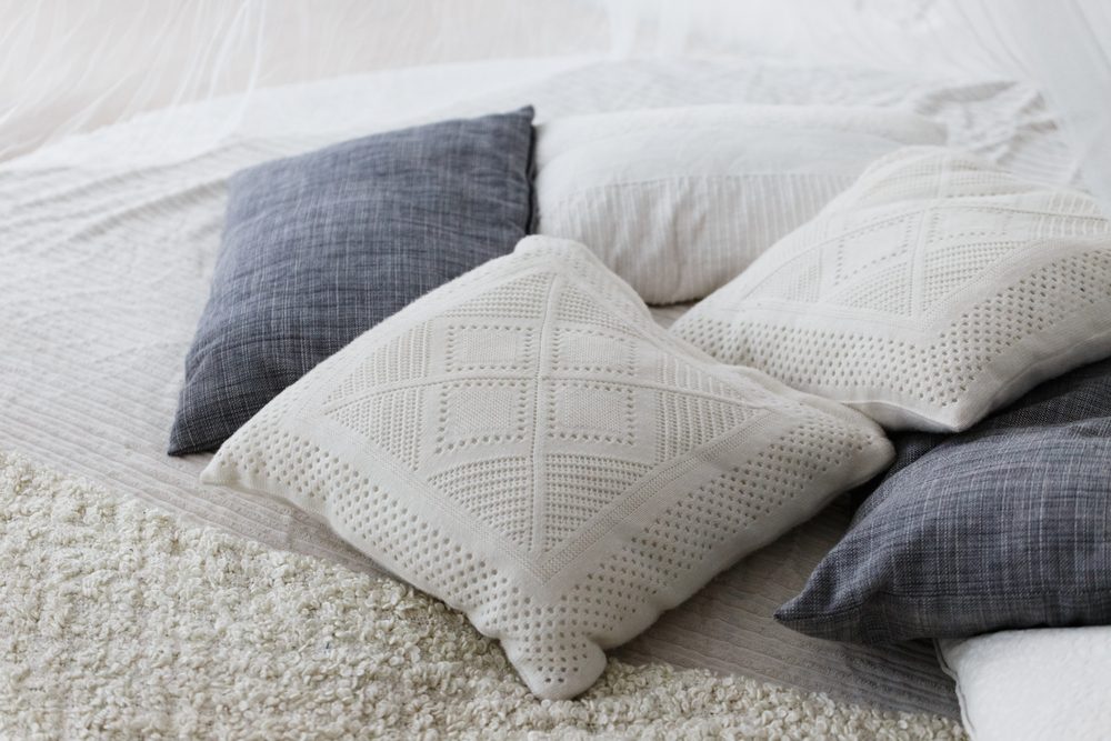 Pastel color, white and light grey cushions or pillows setting on bed with satin bedding style.