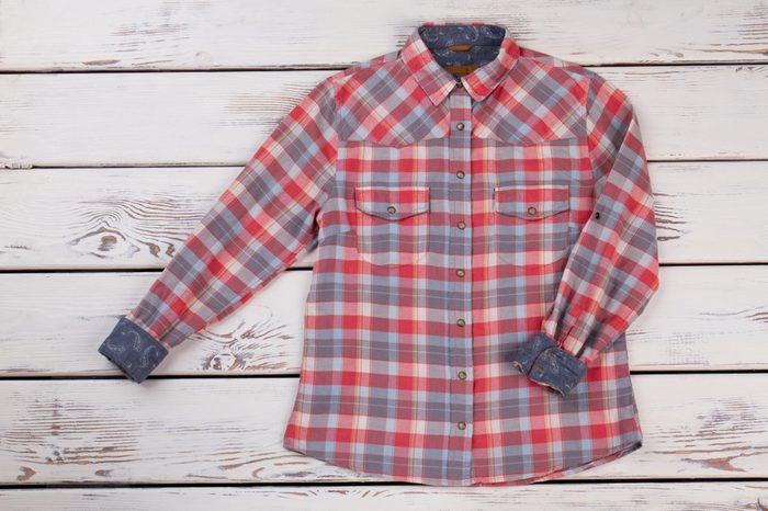 Stylish flannel plaid shirt on wooden shelf. Metal buttons and country pattern. Women's fashion trends.