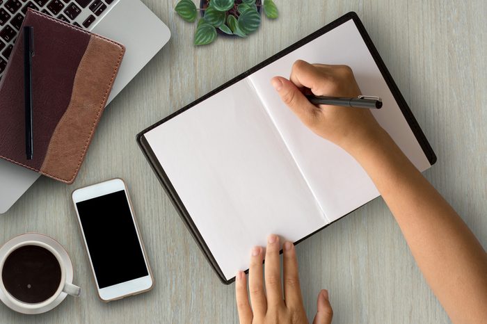 Woman hands writing on book in office.Business woman working on desk of wood.Business woman working with laptop and office supplies on top view.Copy space.