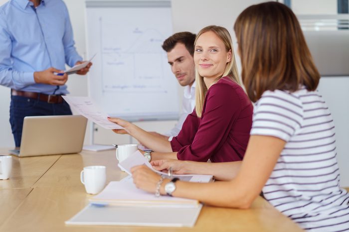 Young business team in a meeting seated around a table in the office with focus to a smiling businesswoman listening to a colleague