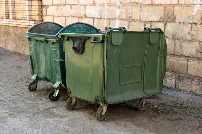 Two Green Trash Dumpsters In Front Of White Brick Wall Angle View in ghetto.