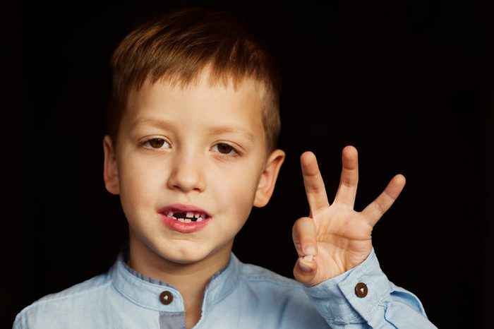 Little smiling child, boy hand showing his first milk or temporary teeth fall out