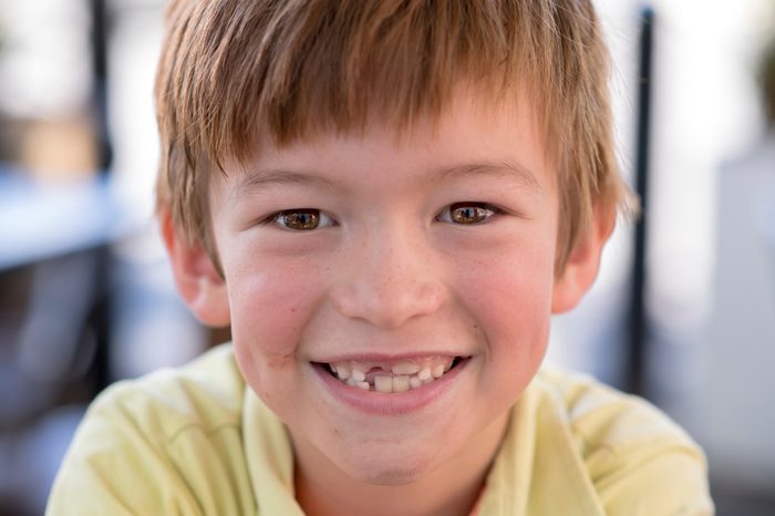 close up headshot portrait of young little 7 or 8 years old boy with sweet funny teeth smiling happy and cheerful in joy face expression looking at the camera in childhood lifestyle concept