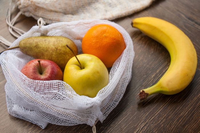 Zero waste, plastic free recycled textile produce bag for carrying fruit (apple, orange, pear and a banana) or vegetables, a wooden surface. Bags are made with a sewing machine out of old curtains.
