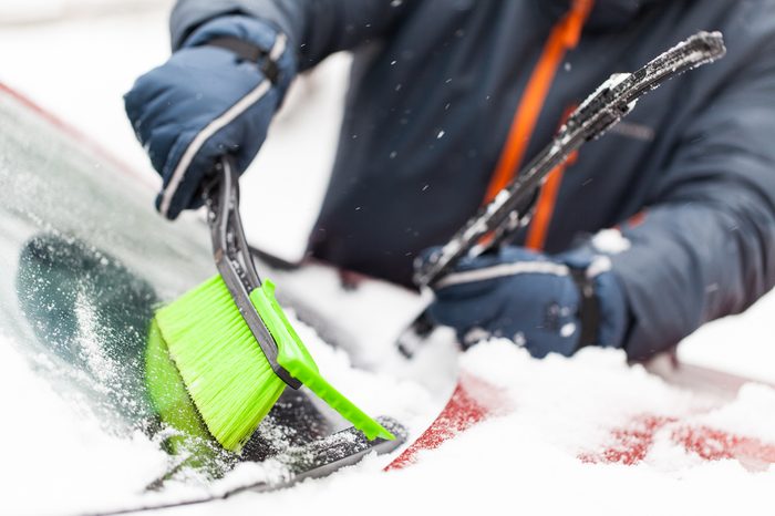 Transportation, winter, weather, people and vehicle concept - man cleaning snow from car with brush