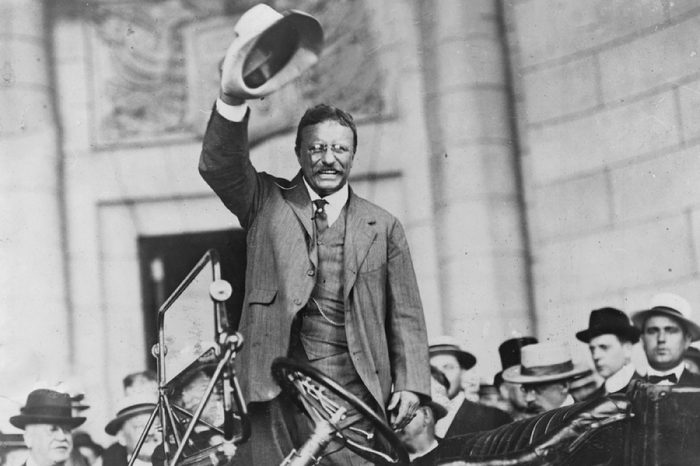 Theodore Roosevelt, waving his hat, as he stands in car. ca.1910.