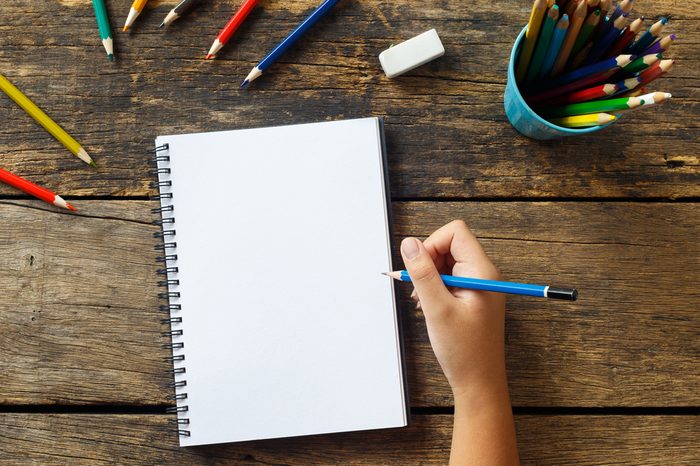 Girl hand drawing, blank paper and colorful pencils on old wooden table