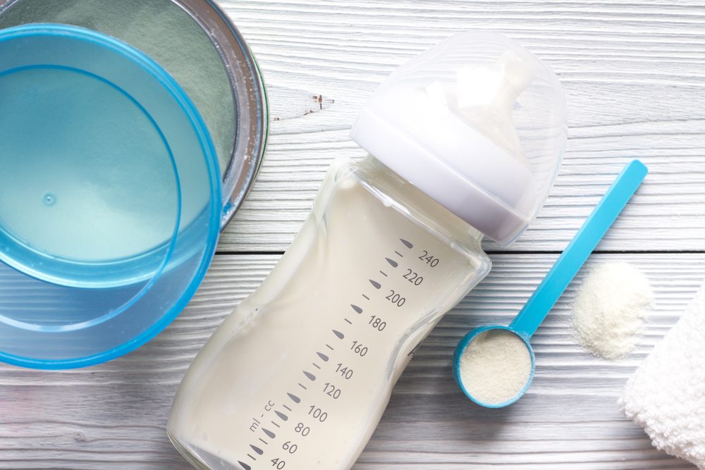 baby formula package, sccop, and bottle on light wood background