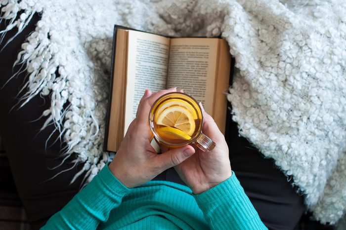 A woman is drinking tea and reading a book, female hands are holding a glass beaker with a drink. Lifestyle, relaxation