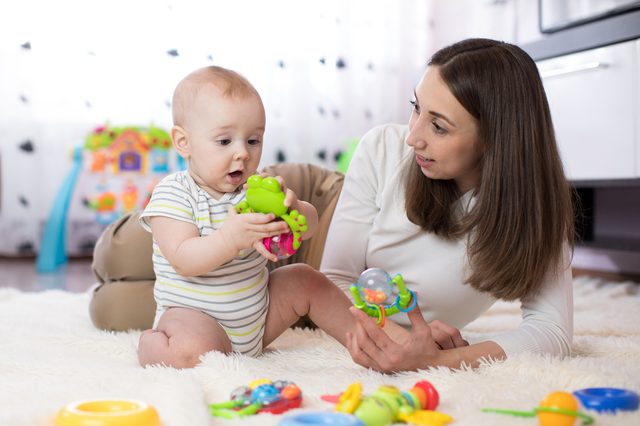 Funny baby boy and young woman playing in nursery. Happy family having fun with colorful toys at home.
