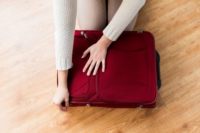 summer vacation, travel, tourism and objects concept - close up of woman packing and zipping travel bag for vacation