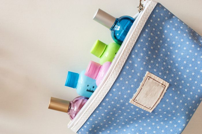 Blue travel toiletry bag with travel toiletries, small plastic bottles of hygiene products and perfume on white background. 