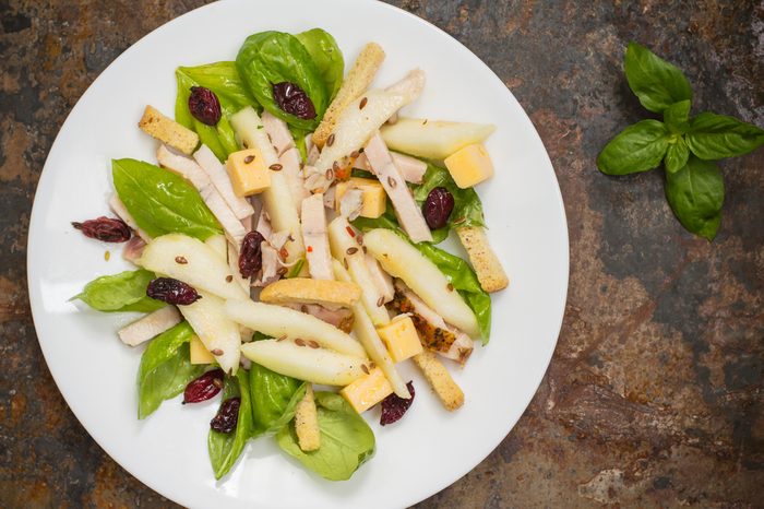 Chicken salad, pears, dried gooseberries and currants, cheese on basil leaves. Wooden background. Top view. Close-up