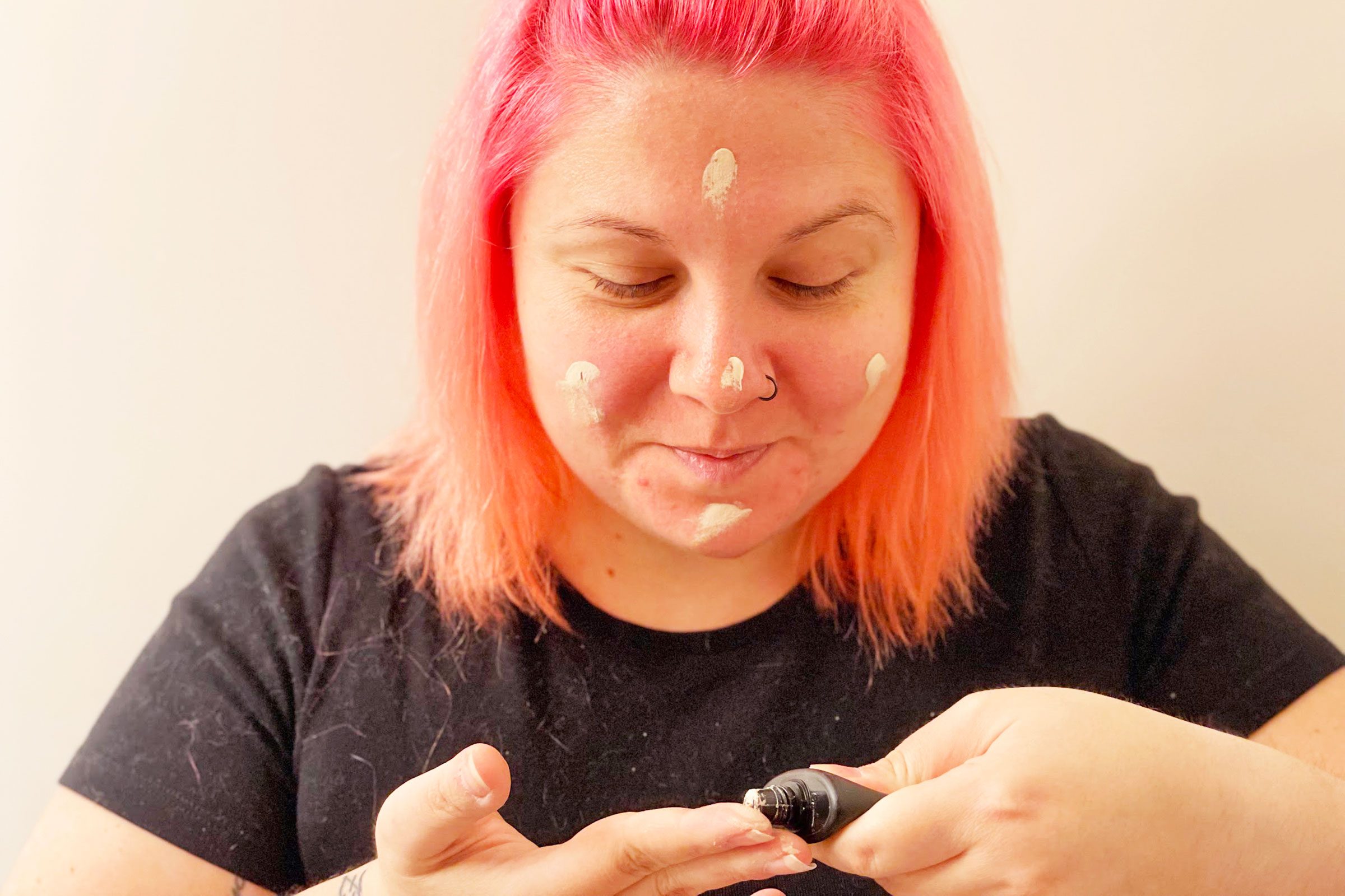 A person applies cream to their face using fingers, with a focused expression in a neutral, indoor setting.