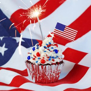 Cupcake topped with a sparkler and U.S. flag sits on an American flag background, decorated with red, white, and blue sugar stars.