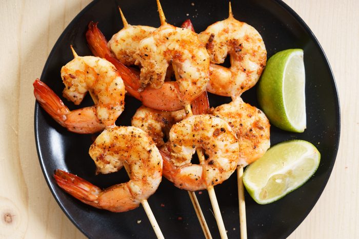 Grilled shrimps on skewer with lime slices and salad