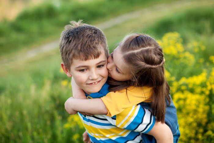 Happy children 5-8 years old, brother and sister, friends, outdoors in summer in a field of blooming yellow flowers, the boy rolls on the back of the girl