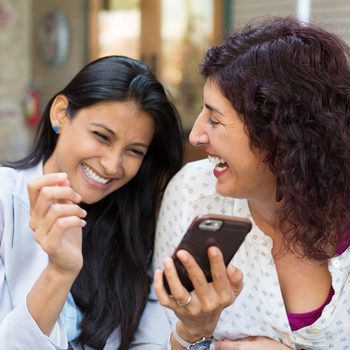 Closeup portrait two surprised girls looking at cell phone, discussing latest gossip news, sharing intimate moments, shopping, laughing at what they see, isolated outdoors background