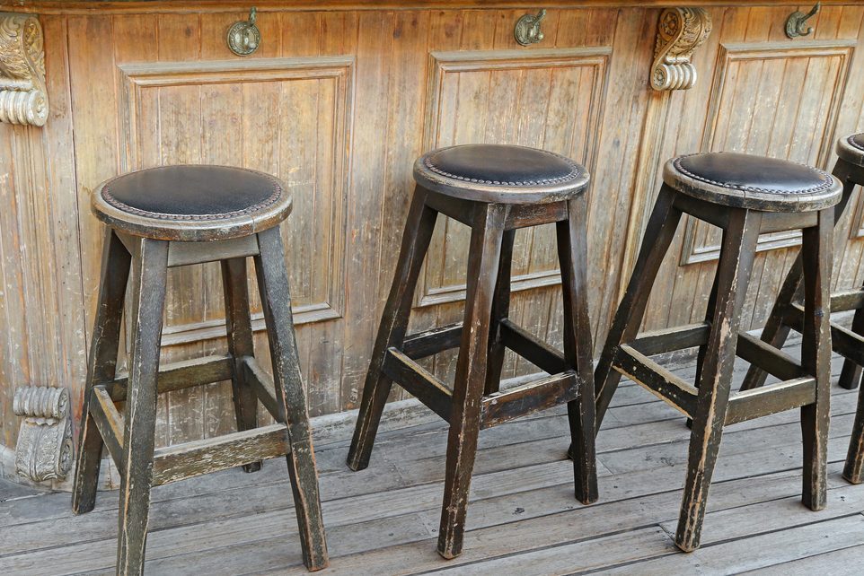 Vintage and rustic wooden bar stools on wooden floor in front of wooden bar with handbag hook hanger
