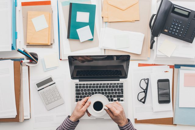 Businessman working at office desk, he is using a laptop and having a relaxing coffee break
