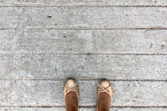 woman wearing flat brown shoes standing on gray cement background.