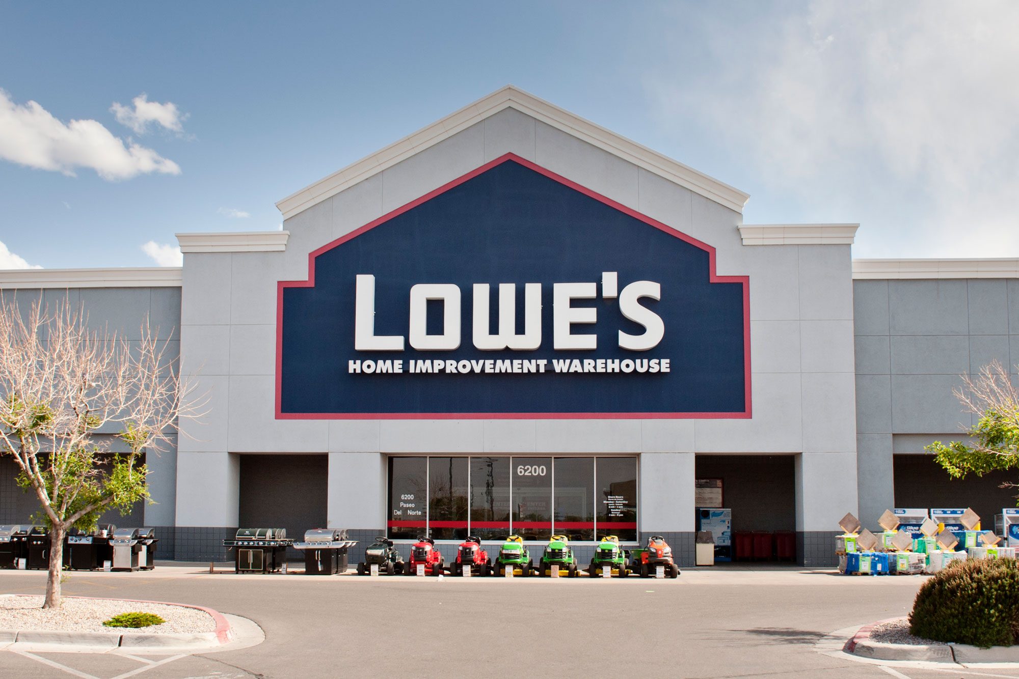 A store displays grills and lawnmowers outside, with "Lowe's Home Improvement Warehouse" on the facade under a cloudy blue sky.