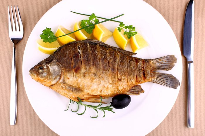 Fried fish on white plate with fork and knife, closeup