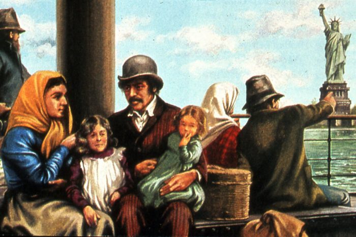 Irish (in tall hats) and European immigrant families arriving in New York harbour and approaching Ellis Island where they would be processed. The Statue of Liberty is in the background. c1900.