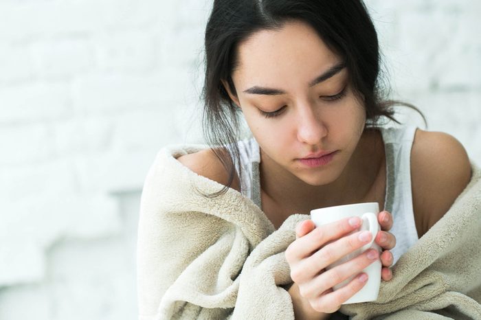 Young woman sick in bed with temperature drinks hot. Indoor shot.