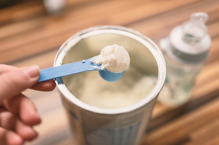 Powder milk and blue spoon on light background close-up. Milk powder for baby in measuring spoon on can. Powdered milk with spoon for baby. Baby Milk Formula and Baby Bottles.