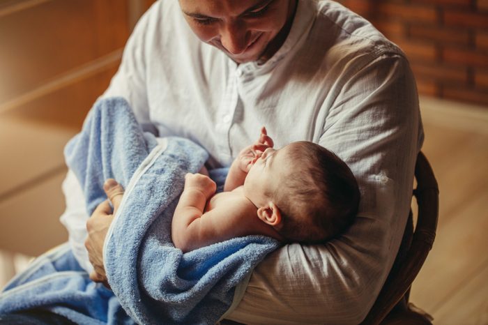 Father With Newborn Baby Working From Home office Using Laptop