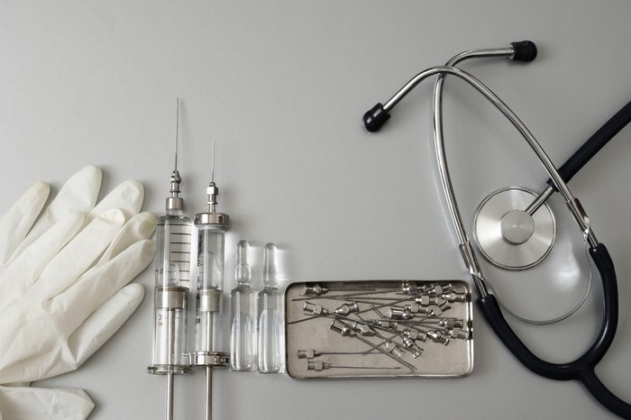 Medical tools: vintage glass syringes, ampules, needles in box, rubber gloves and stethoscope on grey background. Top view point.