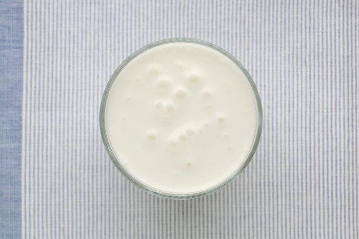 Yogurt or clean white smoothie glass top view on the blue textile background