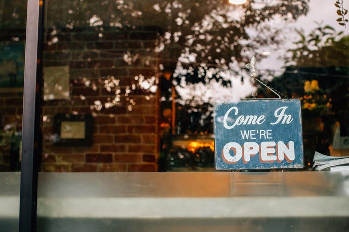 Open sign board close-up through the glass of a window at coffee shop door. Shallow depth of field.