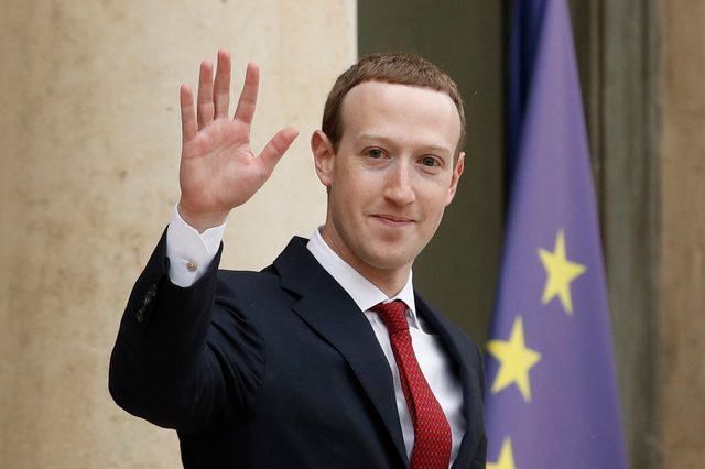 A person in a suit waves, standing beside a European Union flag.