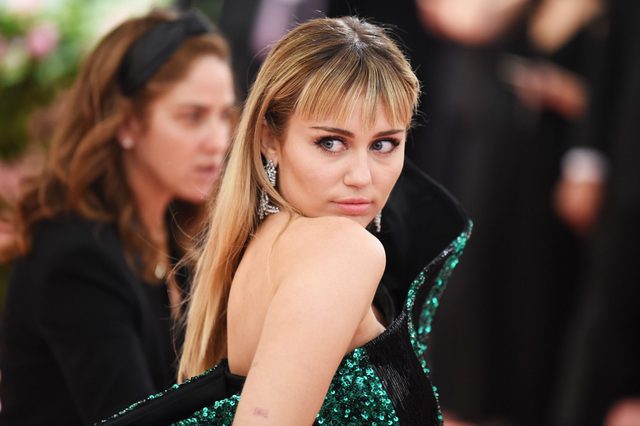 Person glancing over shoulder, wearing emerald sequin dress, in a formal event setting with blurred attendees in the background.