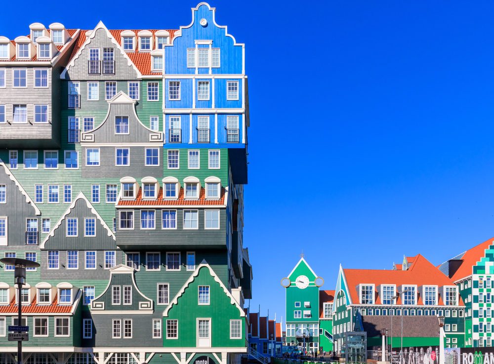 Colorful stacked buildings create an illusion of traditional houses against a clear blue sky, with "hotel" signage visible.