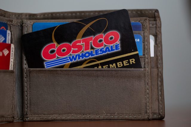 A Costco membership card is partially inserted in a brown wallet, surrounded by various other cards, on a flat surface.