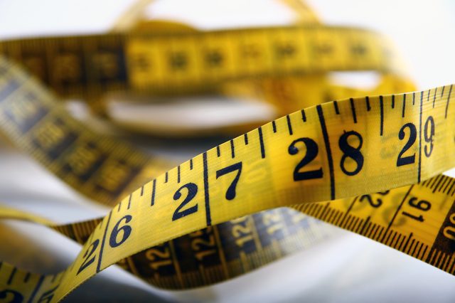 A yellow measuring tape, coiled with numbers visible, lies on a blurred surface, suggesting a sewing or tailoring setting.