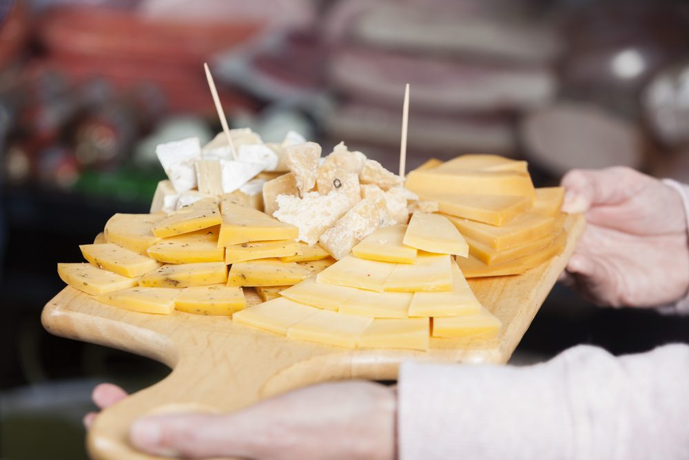 Saleswoman Holding Cutting Board With Various Cheese