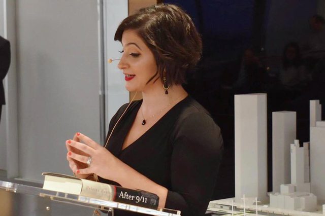 Woman speaking with a headset beside a small-scale architectural model; a book titled "After 9/11" is on the podium.