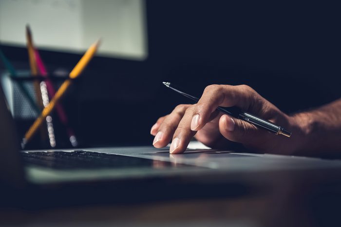 Hand of a man using laptop computer working overtime at his desk in the office late at night