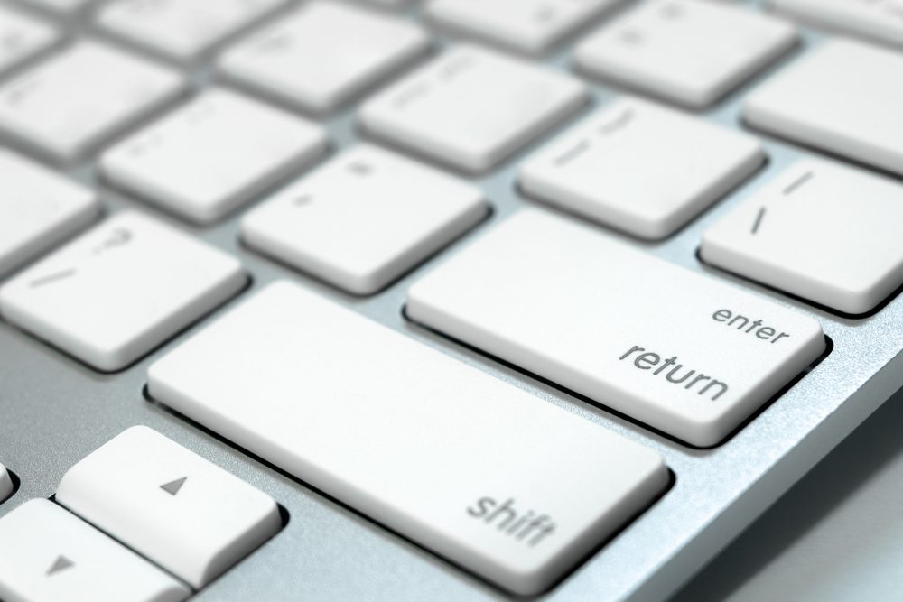 White computer keyboard shows keys including "enter," "return," "shift" with a metallic frame, appearing new and unused.