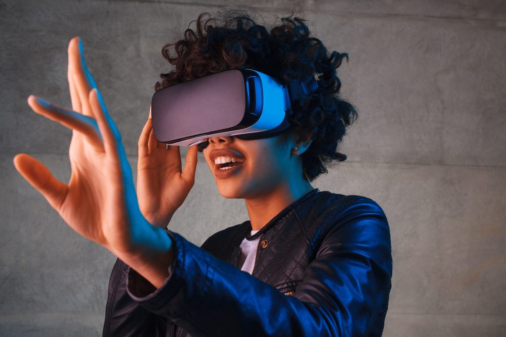Person wearing virtual reality headset, reaching out with hand in a concrete-walled room.