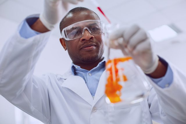 Scientist pours liquid into a beaker, concentrating in a laboratory setting with bright lighting.