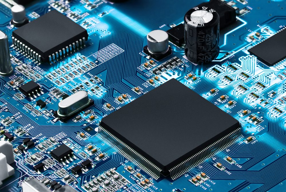 Microchip sits embedded on a blue circuit board, surrounded by intricate pathways and electronic components, including resistors and capacitors.