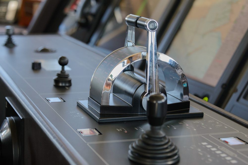 Control lever resting on a sleek black console, surrounded by screens and buttons, likely in a ship's or airplane cockpit.