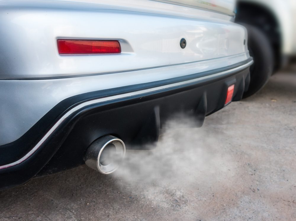 Car exhaust emits smoke, captured close-up, on a concrete surface.