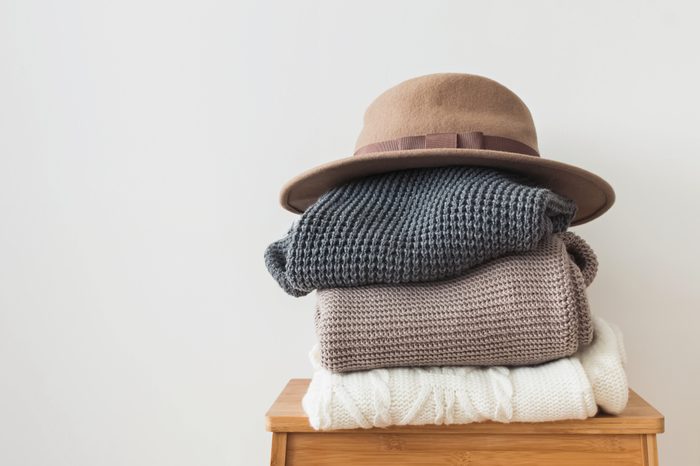 Stack of warm knitted sweater and felt hat on the top of it at the white wall background.